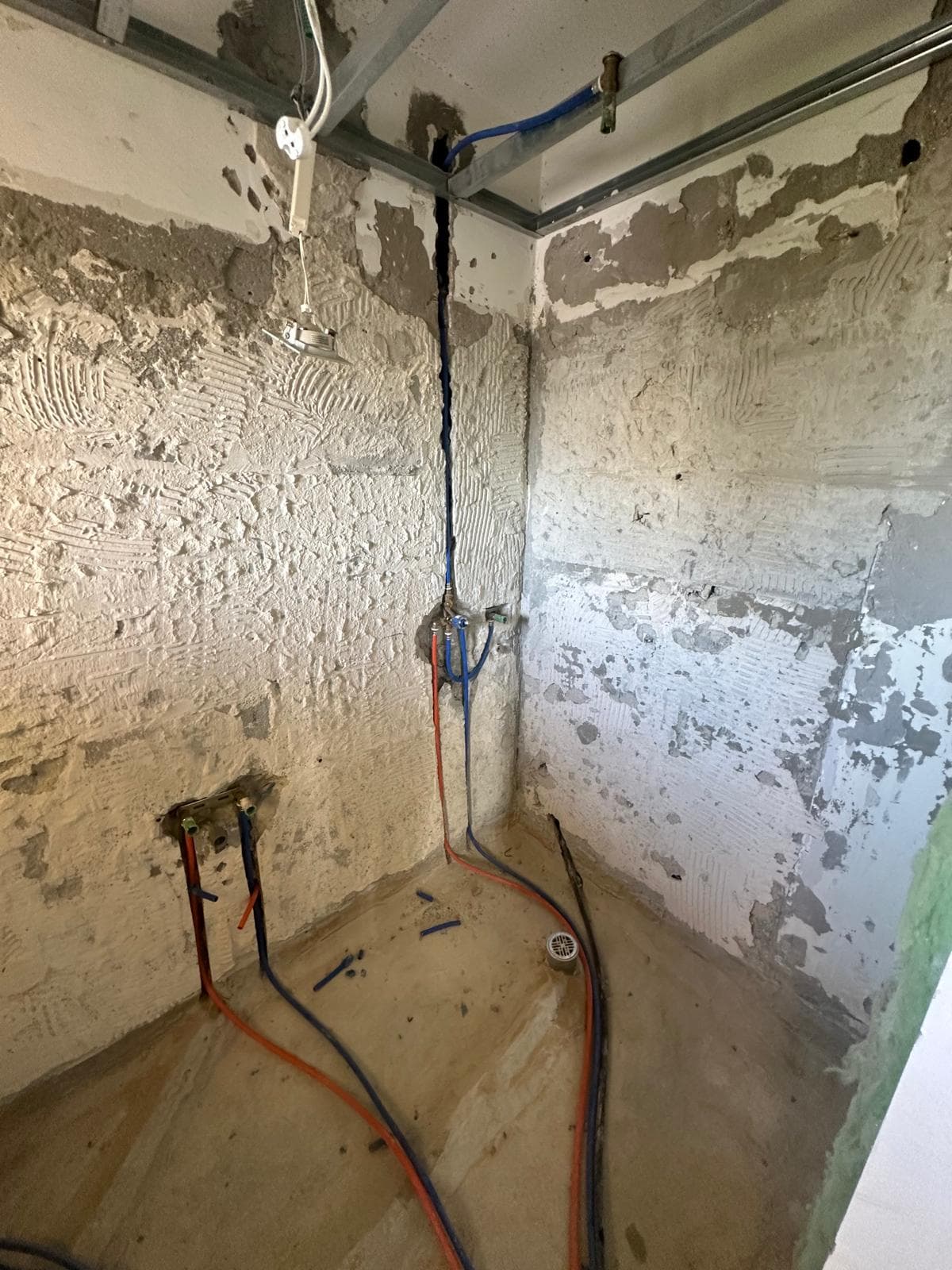 צנרת מים חמים וקרים חדשה פרוסה על רצפת מקלחת, עם שלד מתכת לתקרת גבס